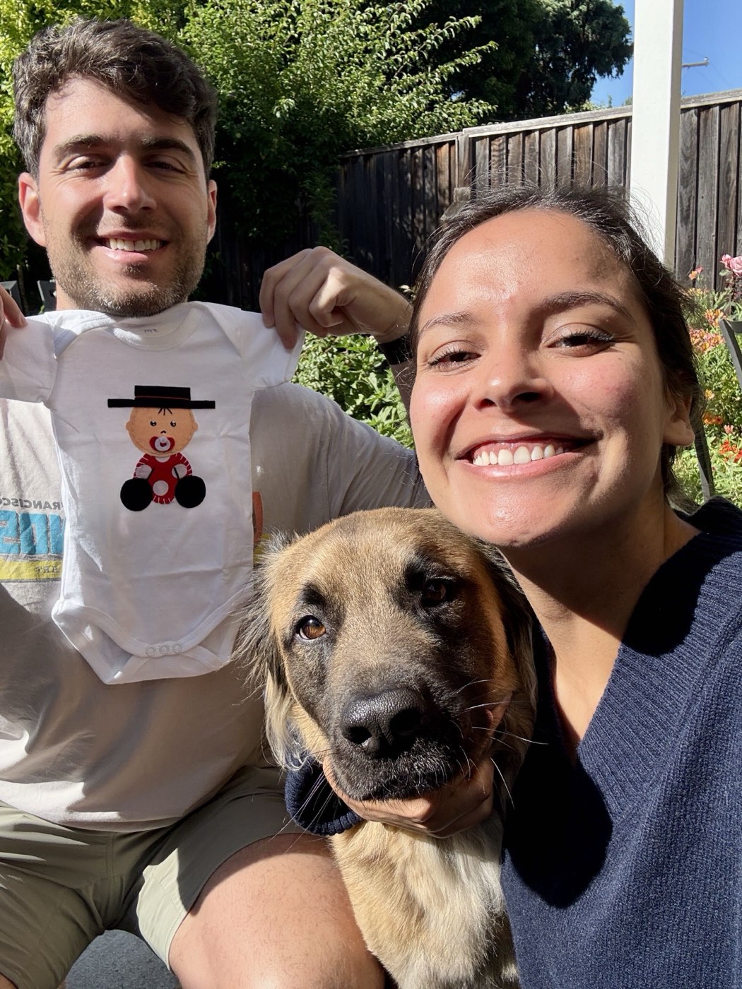 The parents-to-be sharing the happy news with their dog, holding up a onesie